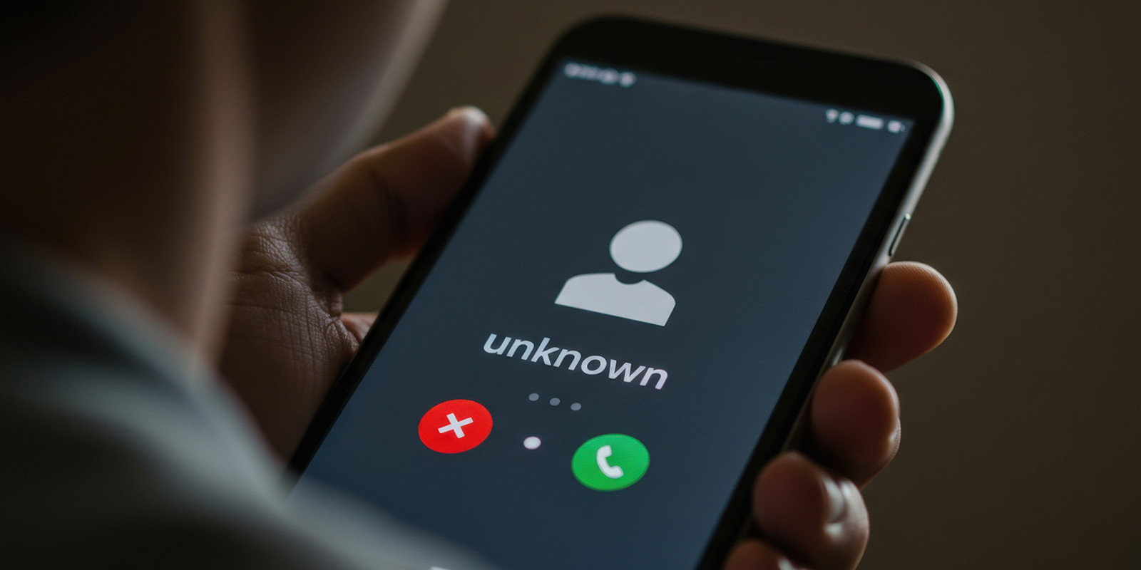 Eine Männerhand hält ein Smartphone, auf dem ein Anruf von einer unbekannten Nummer eingeht