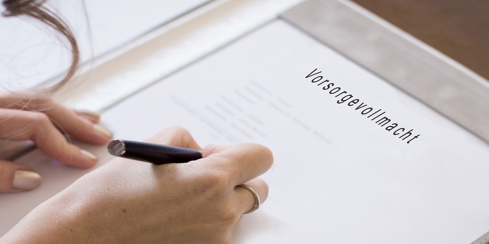 Eine Frau hält einen Stift in der Hand und unterschreibt auf einem Blatt Papier, welches mit Vorsorgevollmacht überschrieben ist