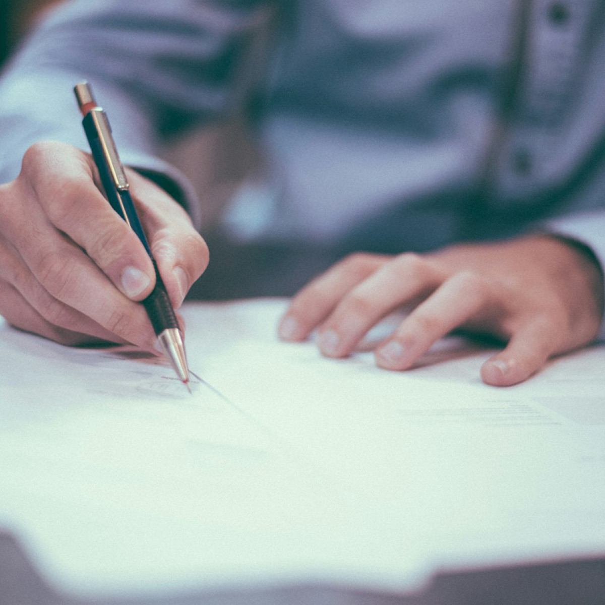 Ein Mann sitzt an einem Tisch, h&auml;lt einen Kugelschreiber in der Hand und pr&uuml;ft ein Dokument