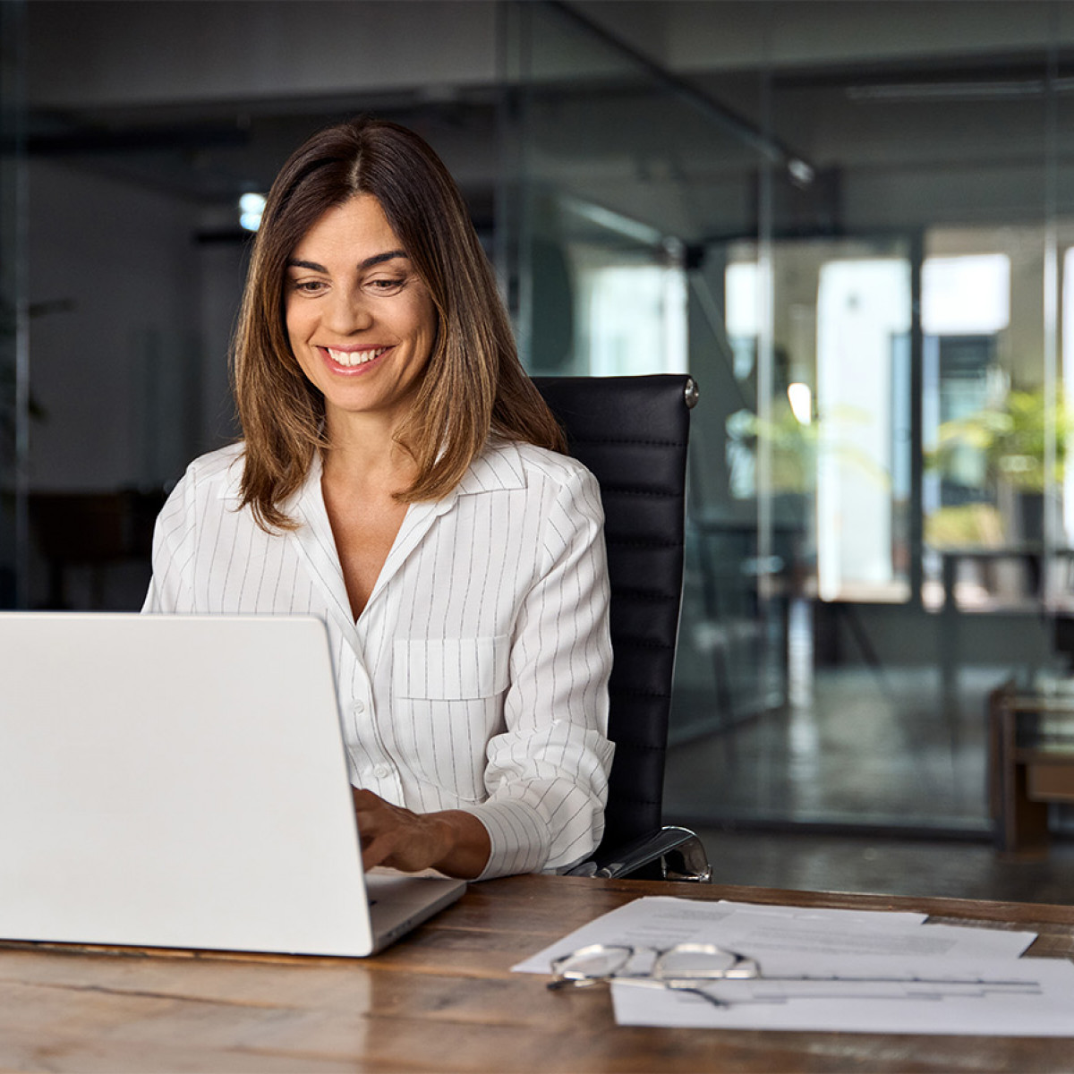 Eine Frau sitzt in einem modernen Büro vor einem Laptop und lächelt