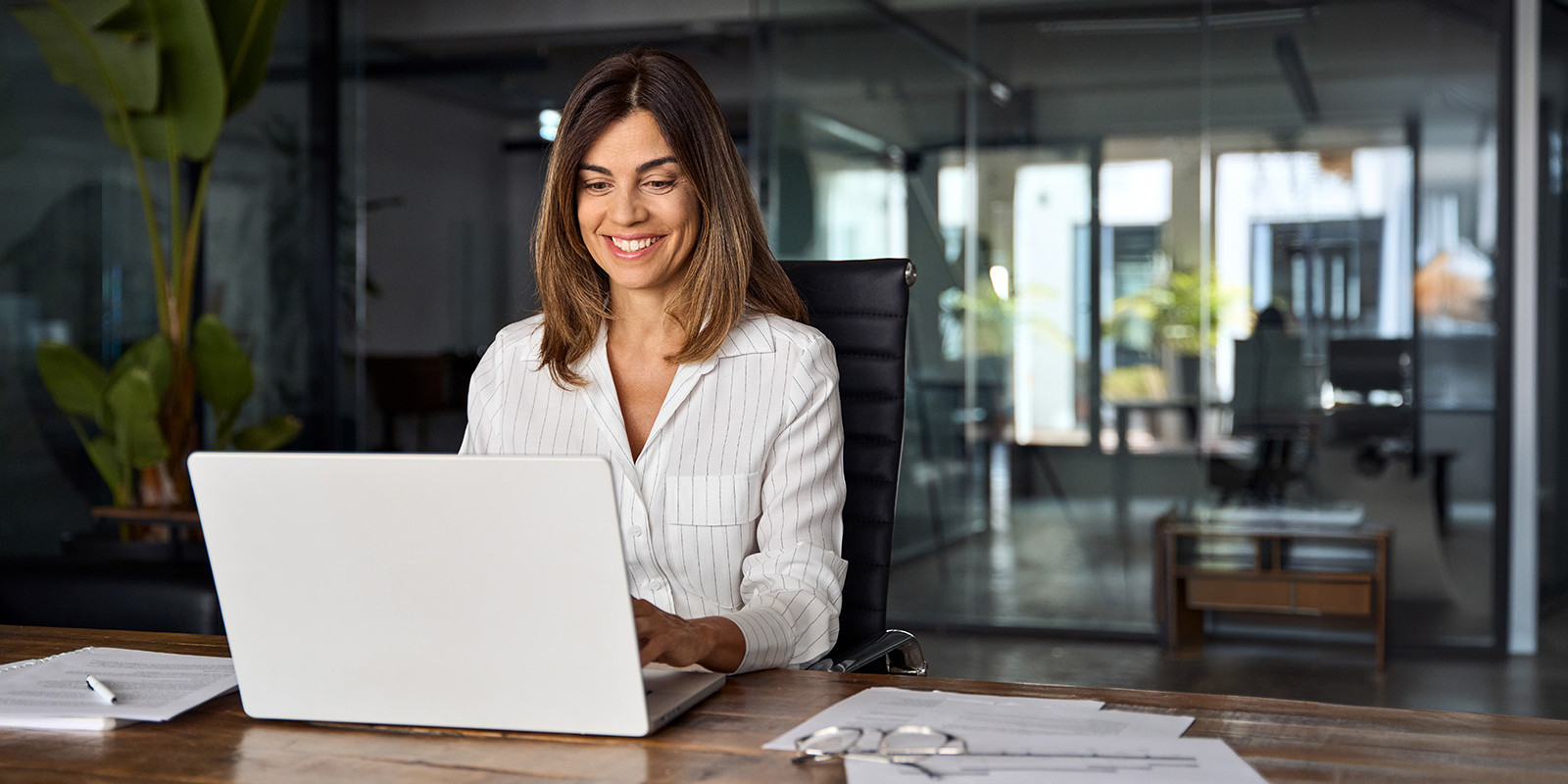 Eine Frau sitzt in einem modernen Büro vor einem Laptop und lächelt