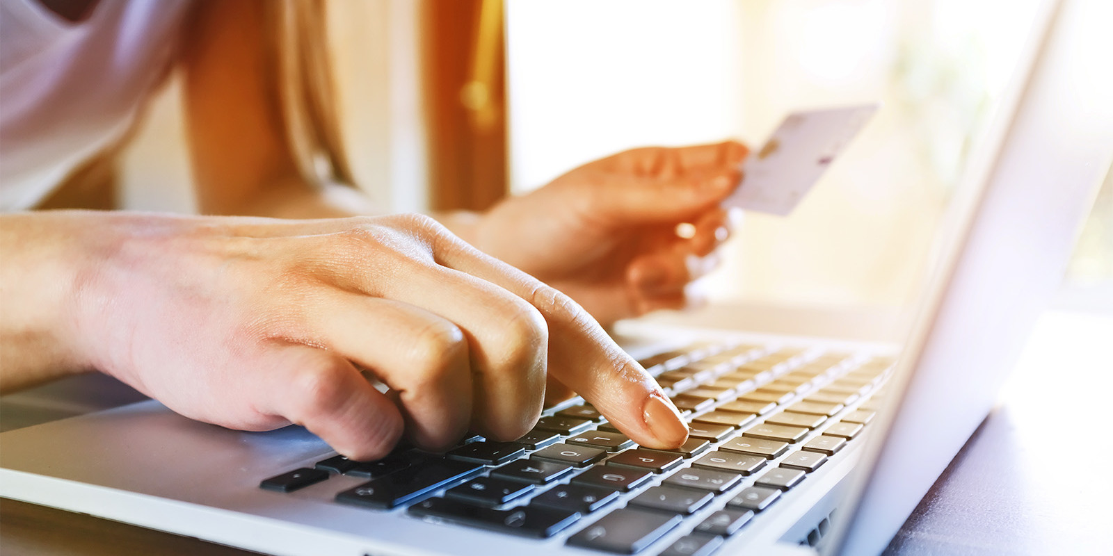 Man sieht die Hände einer Frau, die gerade ihre Kreditkarte in der Hand hält und eine Transaktion am Laptop ausführt